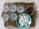 A decorative metal tray holds a set of six clear wine glasses with floral etchings. Beside them, a glass square dish contains assorted olives. A turquoise bowl filled with white, round rice crackers is also placed on the tray.