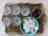 A decorative metal tray holds a set of six clear wine glasses with floral etchings. Beside them, a glass square dish contains assorted olives. A turquoise bowl filled with white, round rice crackers is also placed on the tray.