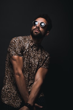 man wearing brown and black leopard print button-up T-shirt and black sunglasses crossing hands down while looking up