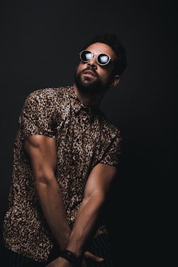 man wearing brown and black leopard print button-up T-shirt and black sunglasses crossing hands down while looking up
