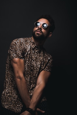 man wearing brown and black leopard print button-up T-shirt and black sunglasses crossing hands down while looking up
