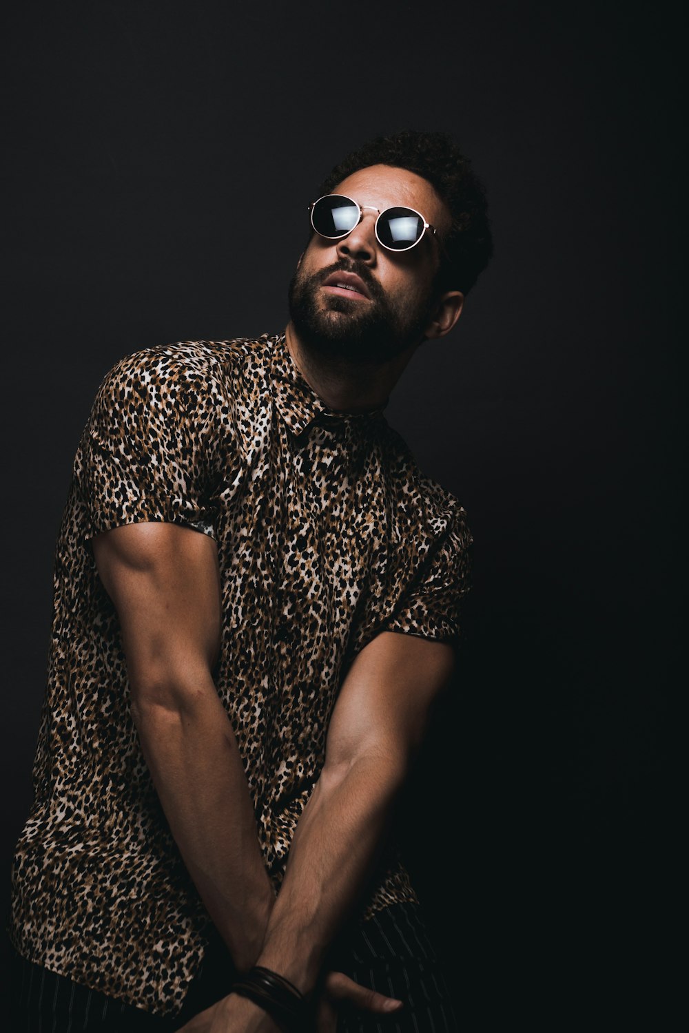 man wearing brown and black leopard print button-up T-shirt and black sunglasses crossing hands down while looking up