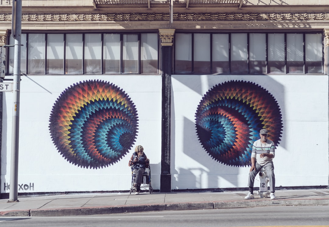 two men sitting near white wall painting during daytime