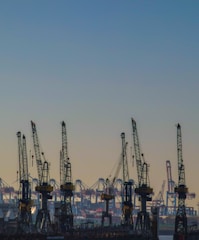 Several large cranes are visible at a port or dockyard, with numerous other cranes and industrial structures in the background. The sky is clear, giving the scene a sense of openness and space.