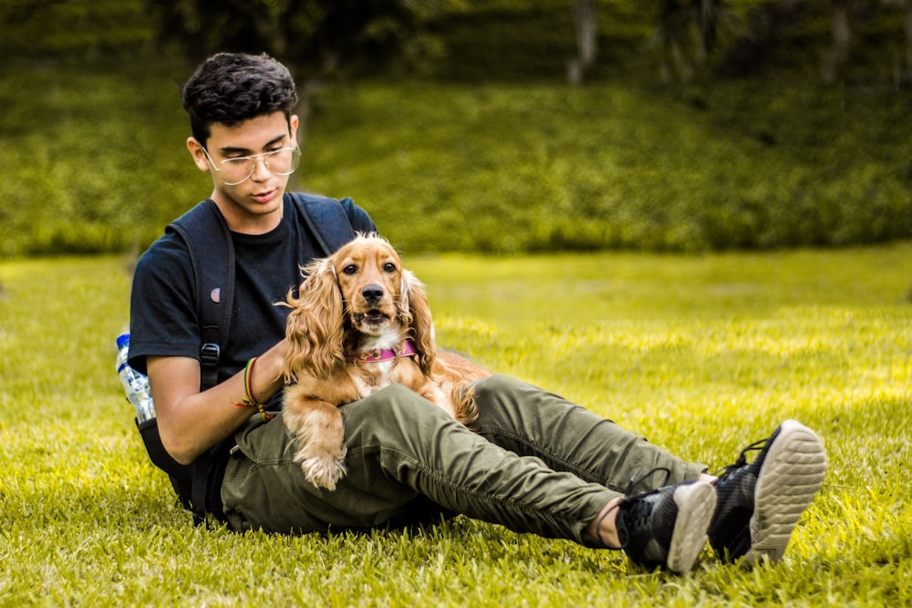 homme caressant un chien brun à poil long tout en étant assis sur un sol couvert d’herbe verte pendant la journée