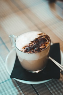 Classic cappuccino topped with a dusting of cocoa powder, served with a silver spoon on a saucer.