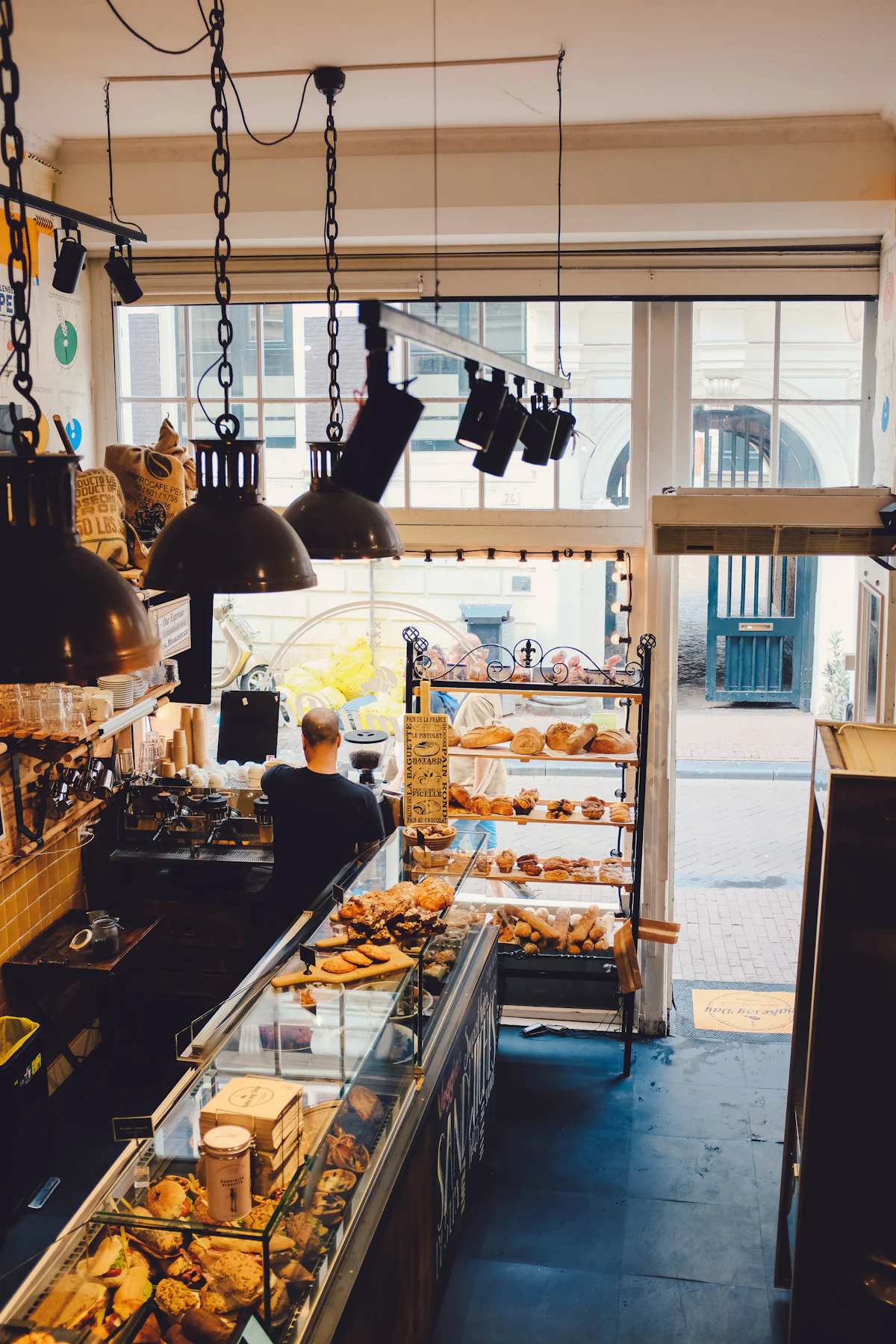 L'intérieur d'une boulangerie avec sa vitrine de viennoiseries et un boulanger derrière le comptoir, porte ouverte sur la rue