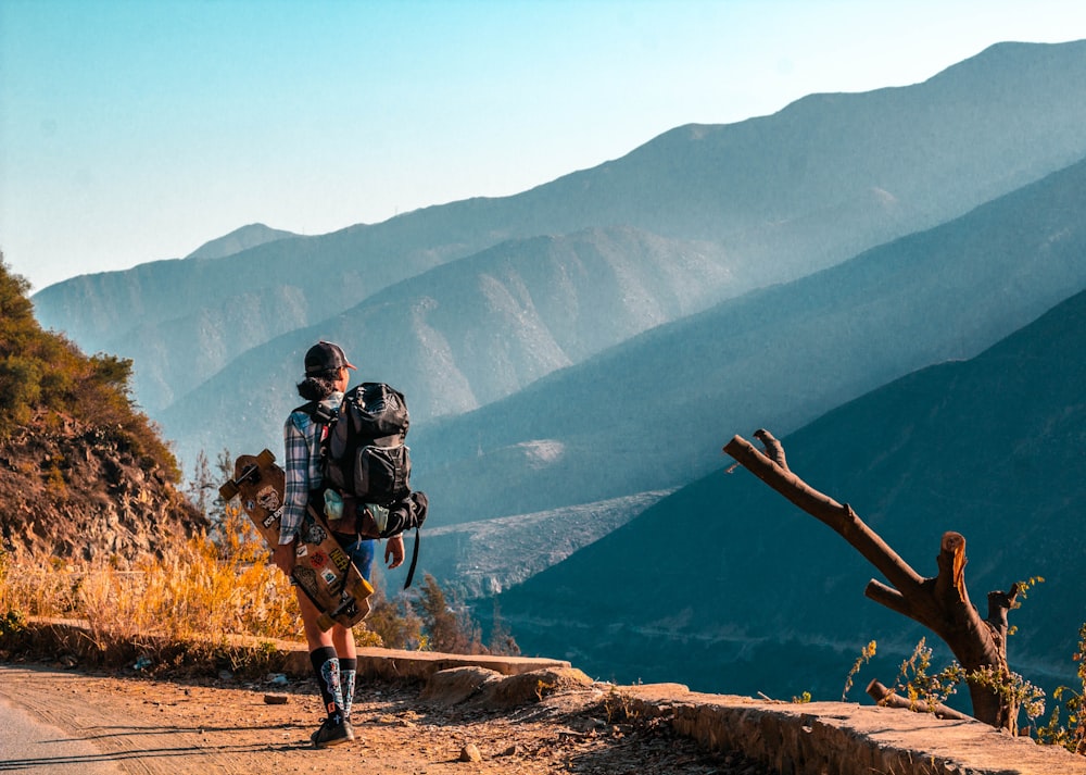 woman carrying longboard while carry backpack staring at mountains