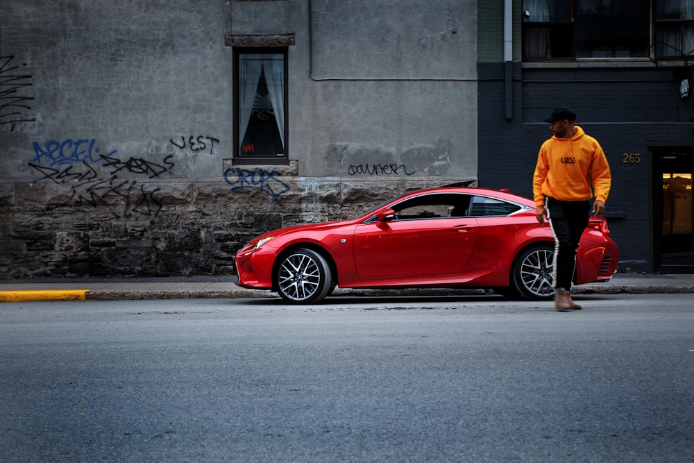 man standing near red coupe on side of street