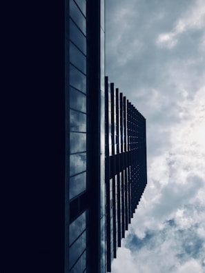 A striking perspective of a modern high-rise building captured from below, with its dark reflective facade contrasting against a cloudy sky.