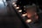 A power strip with several electronic devices plugged in, illuminated by small orange indicator lights. The scene is dimly lit, casting a shadowy atmosphere over a wooden surface.