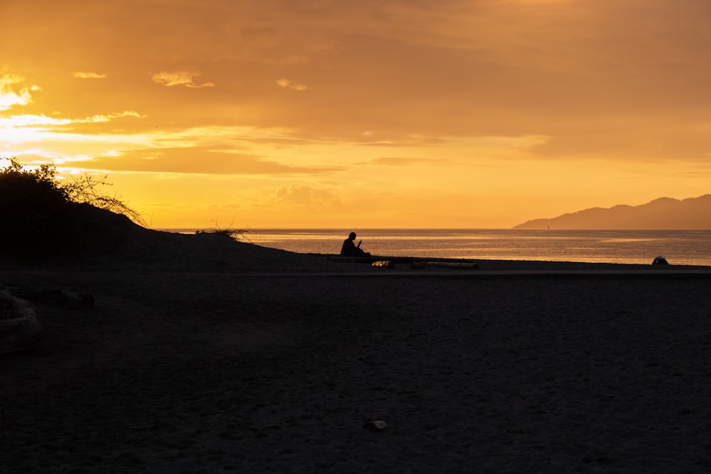 silhouette of man sitting on beach during golden hour