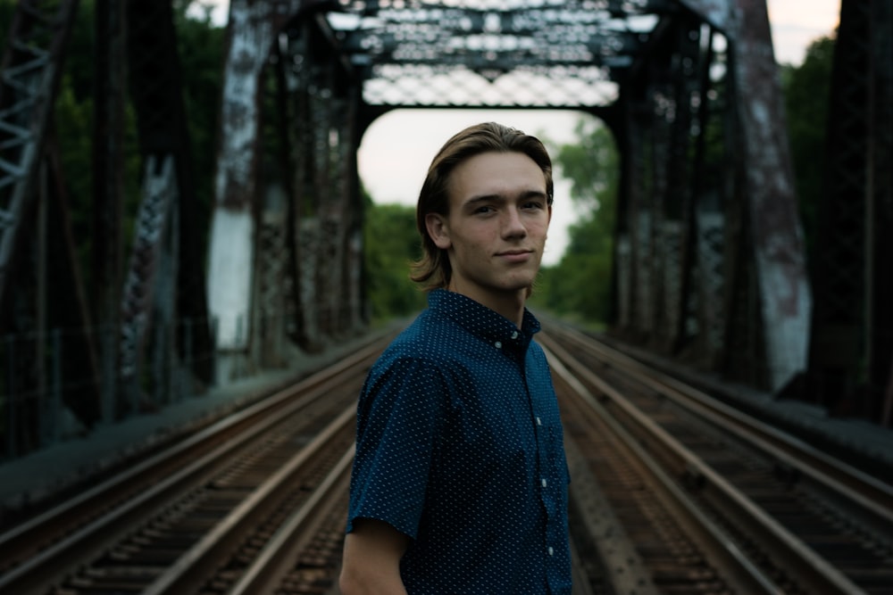 man wearing blue collared button-up shirt standing on railway