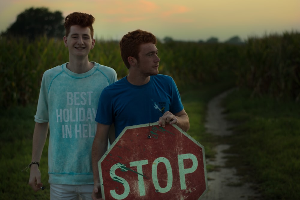 man standing beside man holding stop signage near green grasses during daytime