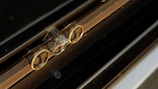 Three rings are arranged with two gold bands flanking a central engagement ring, featuring a prominent square-cut diamond. The rings are positioned on a glass or reflective surface with a dark background, which creates a mirrored effect.