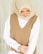 A woman wearing a beige hijab and a brown sleeveless vest over a white shirt. She is looking down with a serene expression, and her hands are gently clasped in front of her.