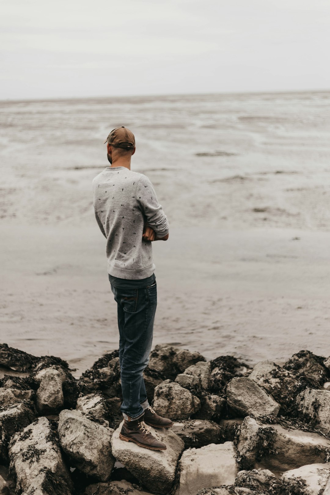 man standing on rocks facing the sea