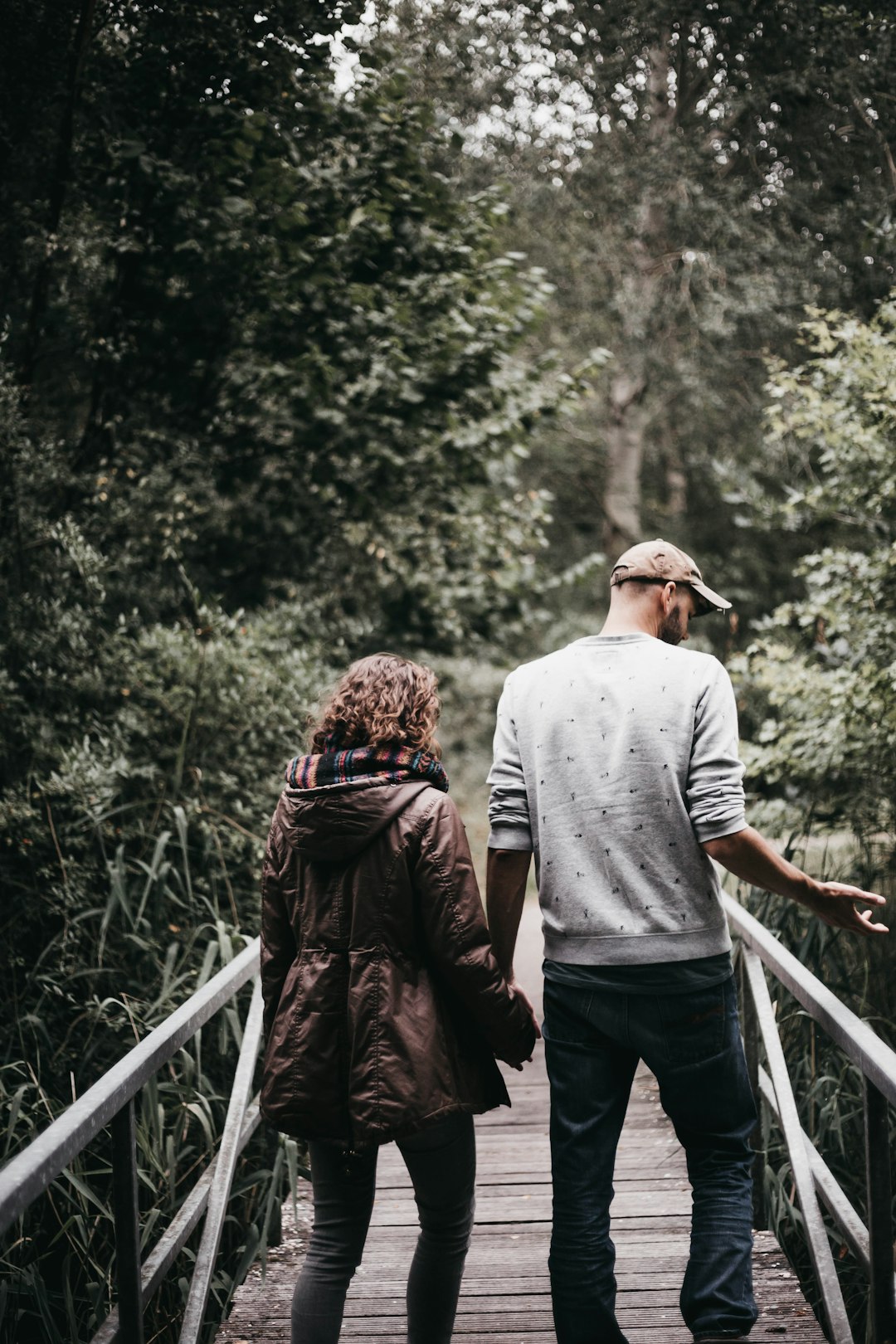 man and woman holding hands walking on bridge during daytime