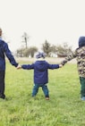 three children holding hands standing on grasses