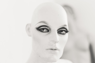 A mannequin head with stylized makeup, featuring dramatic eyeliner and bold eyebrows, set against a blurred background.