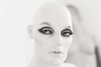 A mannequin head with stylized makeup, featuring dramatic eyeliner and bold eyebrows, set against a blurred background.