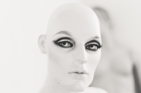 A mannequin head with stylized makeup, featuring dramatic eyeliner and bold eyebrows, set against a blurred background.