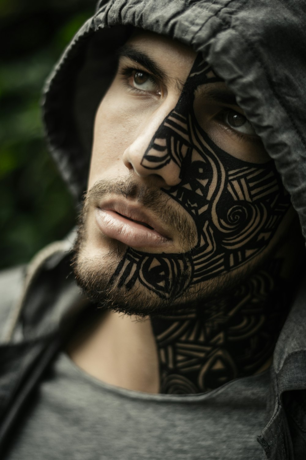 Mann mit Gesichtstätowierung trägt grauen Kapuzenpullover