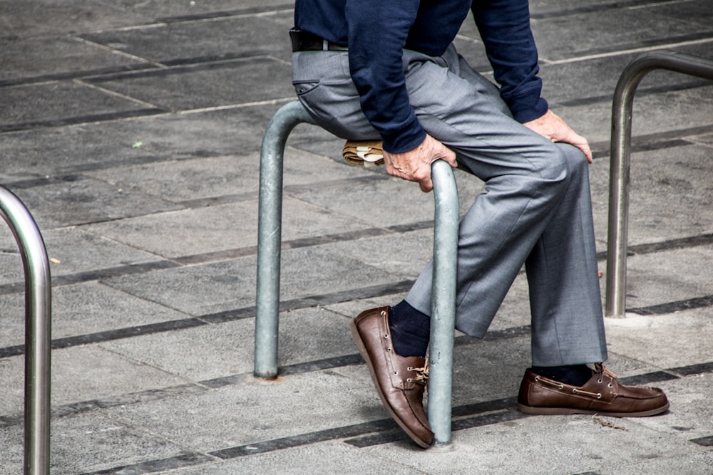 homme assis sur un arceau de sécurité en métal gris sur un trottoir gris