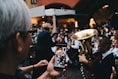 selective focus photo of woman holding phone taking a photo of man playing instrument