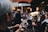 A person is taking a photo of a brass band performance using a smartphone. The band members are wearing uniforms and playing musical instruments such as trumpets and tubas. The scene is crowded, possibly at an outdoor event, with people gathered closely together.