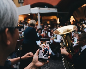 selective focus photo of woman holding phone taking a photo of man playing instrument