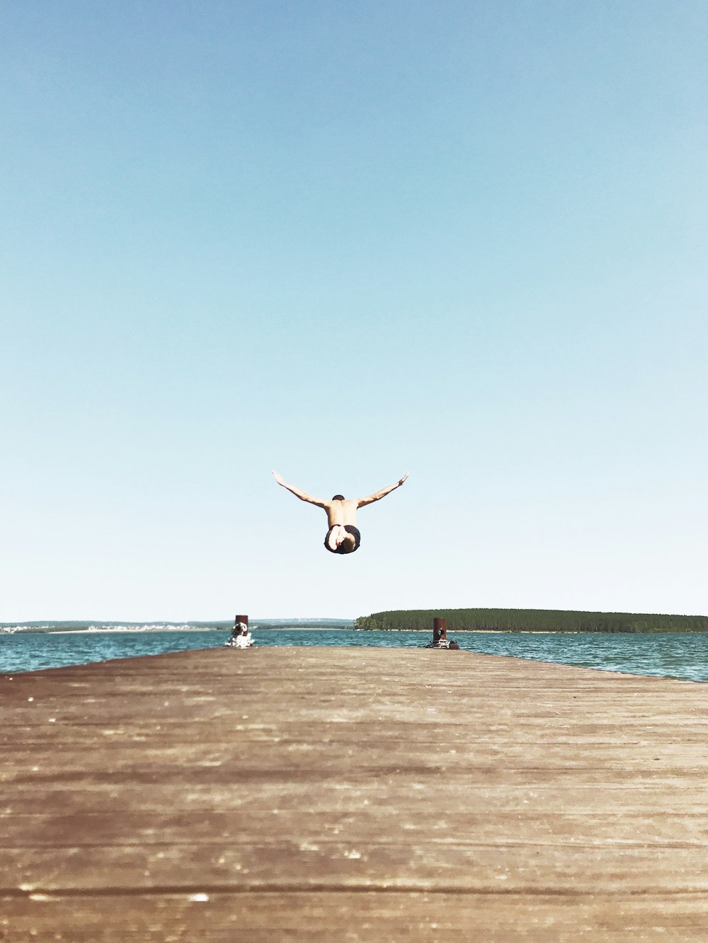 man on air while spreading both hands above body of water under blue sky during daytime