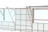 A metallic structure with a mesh-style railing and horizontal and diagonal beams. The background features a bright and overexposed sky, suggesting an industrial or construction setting.