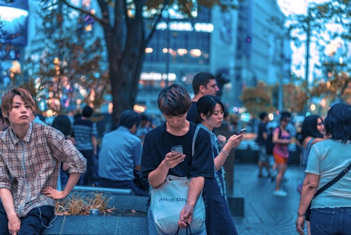 selective focus photography of man sitting on concrete chair while holding smartphone