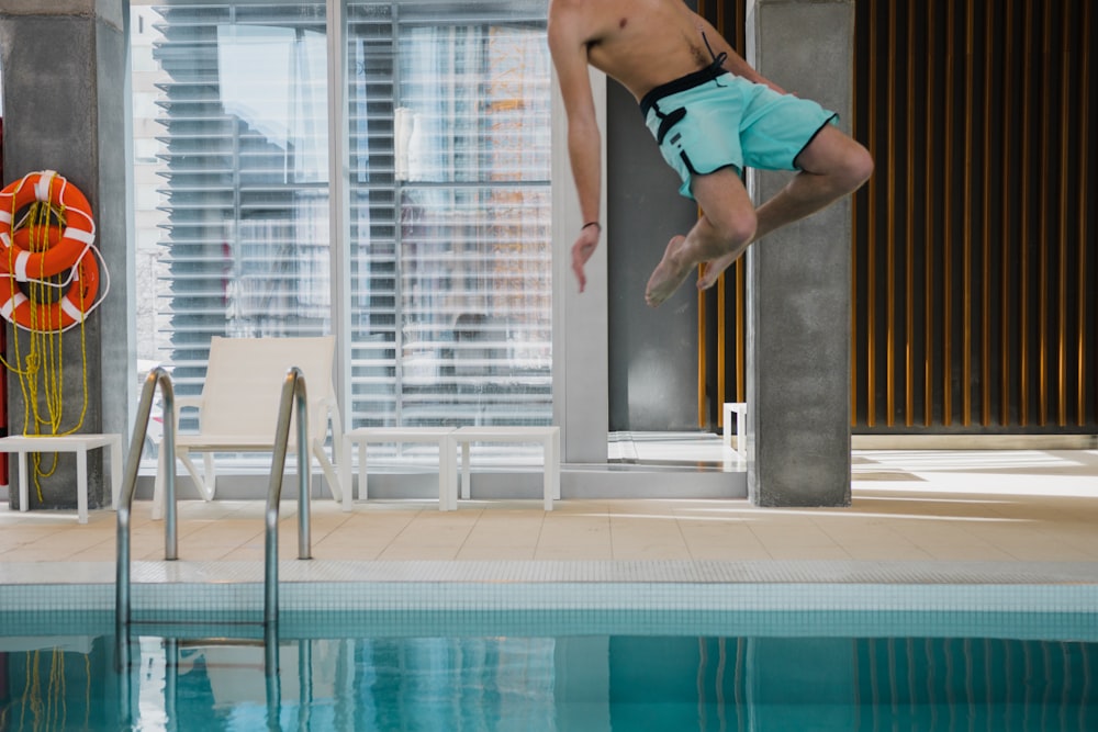 Mann in blaugrünen Boardshorts springt auf Pool