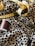 Detailed view of a sewing setup including a leopard print fabric, a yellow measuring tape, a spool of brown thread, and a pair of metal scissors.
