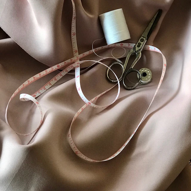 White tape measure and gray tailoring scissors on a green surface