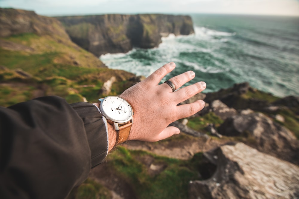 selective focus photo of left human hand wearing round white and silver-colored analog watch with brown leather strap