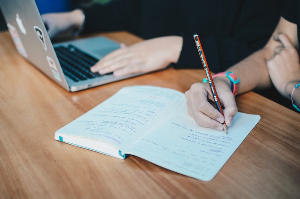 two person using MacBook and holding pencil