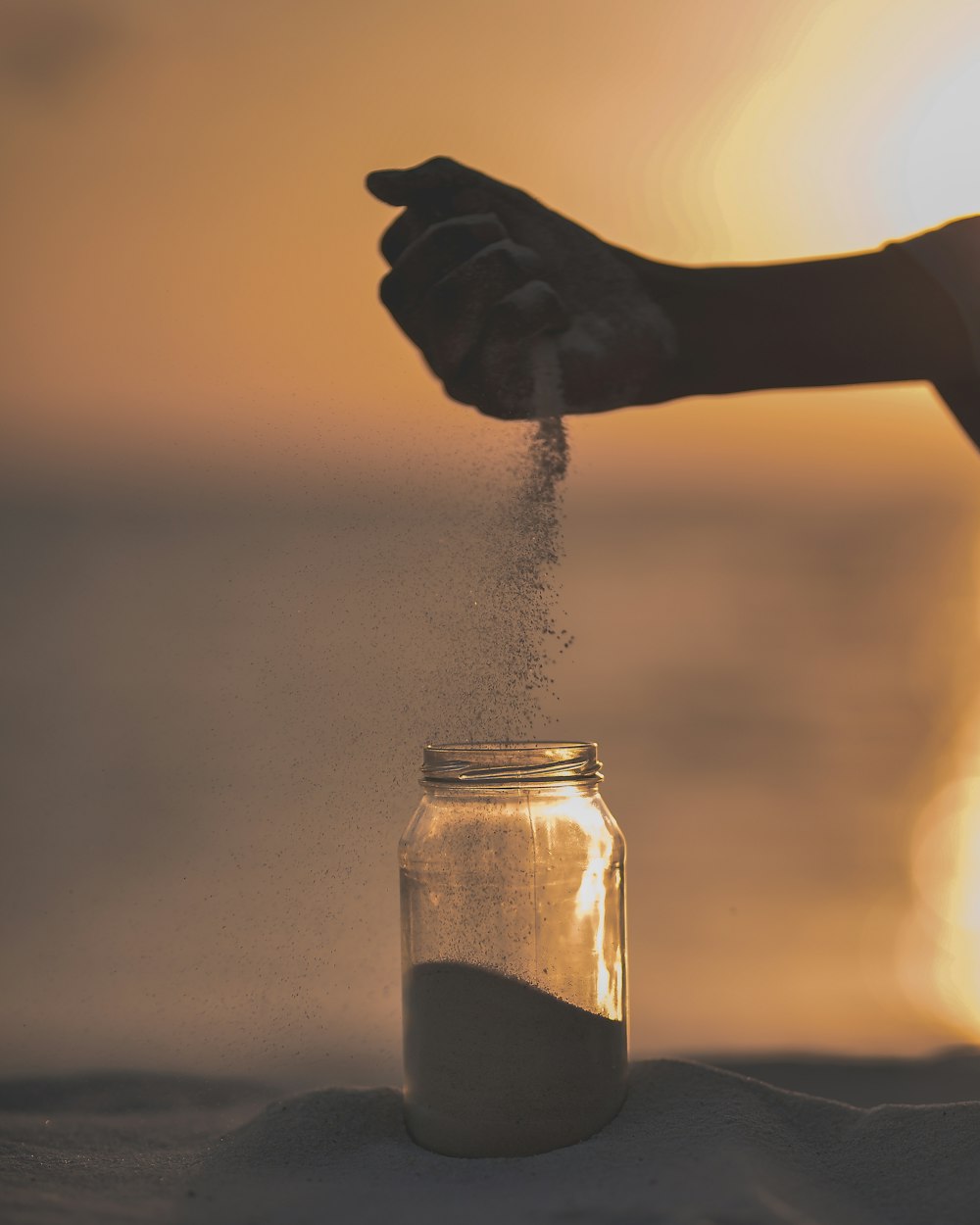 person holding sand putting on clear glass jar