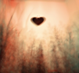 A blurred and abstract background with warm earthy tones, featuring a prominent black heart shape in the center. The overall texture appears soft and dreamlike, evoking a sense of depth and mystery.