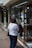 Two people are standing outside a shop with a glass display window. The window is adorned with various payment method stickers, including those for Visa and Mastercard. The individuals appear to be engaged in conversation, and one is wearing a white shirt and holding a black bag.