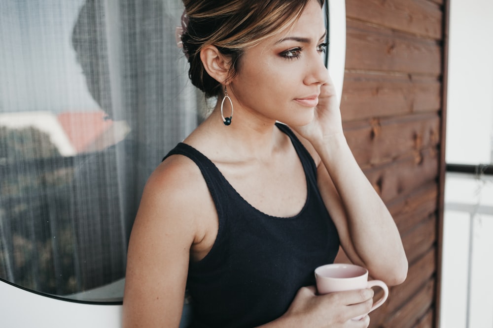 donna che indossa una canotta nera che tiene la tazza