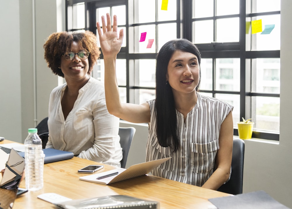 woman sitting raising her hand beside woman