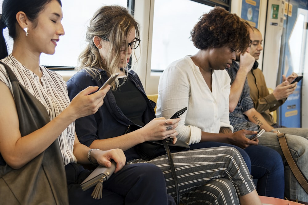 three women holding smartphone sitting on train