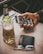 A hand is holding a smartphone displaying a social media app with images. A bottle of beer with a filled glass sits next to a black wallet and a pair of glasses on a wooden table.