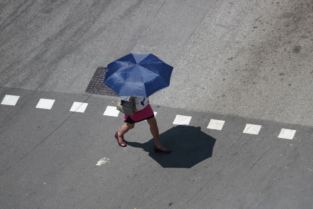 woman under blue umbrella walks on gray concrete pavement