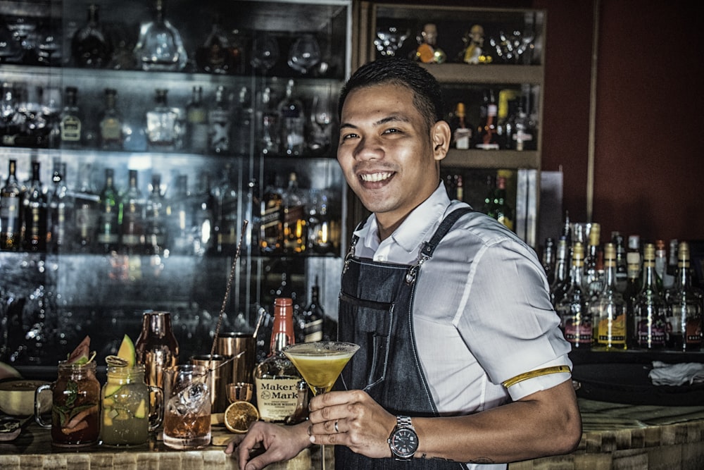Hombre sonriendo mientras sostiene una copa de martini llena de líquido amarillo