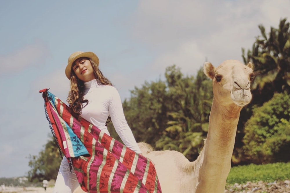 selective focus photography of woman standing beside brown camel during daytime