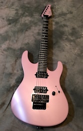 A sleek, pink electric guitar with a glossy finish is positioned on a textured gray background. It features a double cutaway body, black pickups, and tuning pegs. The strings and control knobs are clearly visible, with detailed craftsmanship on the bridge and fretboard.